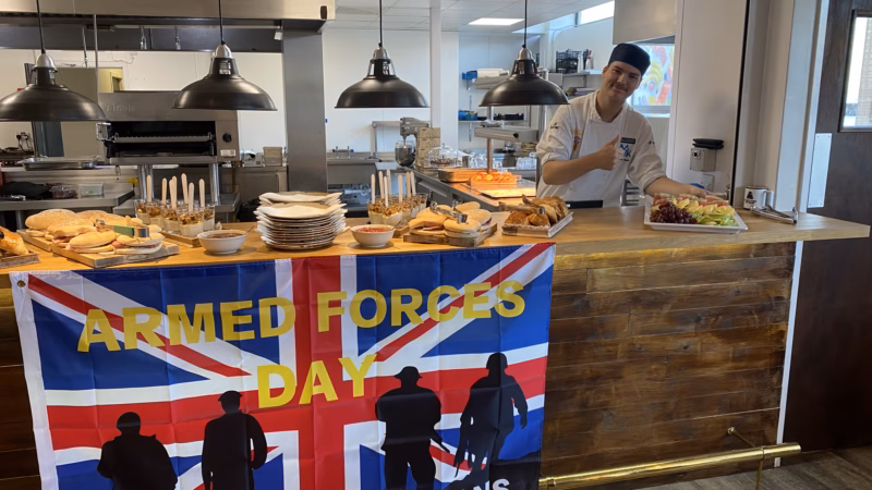 Student from MK College stands in front of an array of breakfast items for the College's Armed Forces breakfast at The Brasserie.