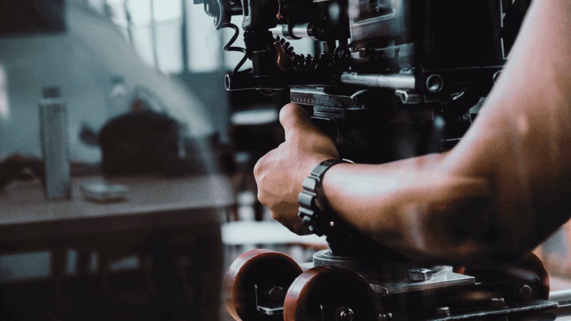 A person operating a professional video camera mounted on a wheeled tripod inside a studio or workspace.