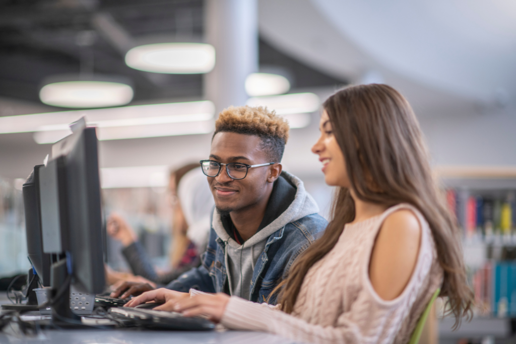 2 students sat behind a computer looking at the screen together