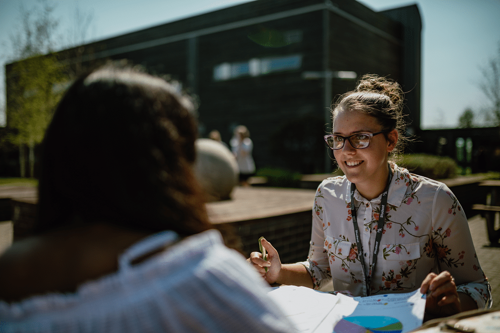 2 students sat outside talking together while working through their textbooks.
