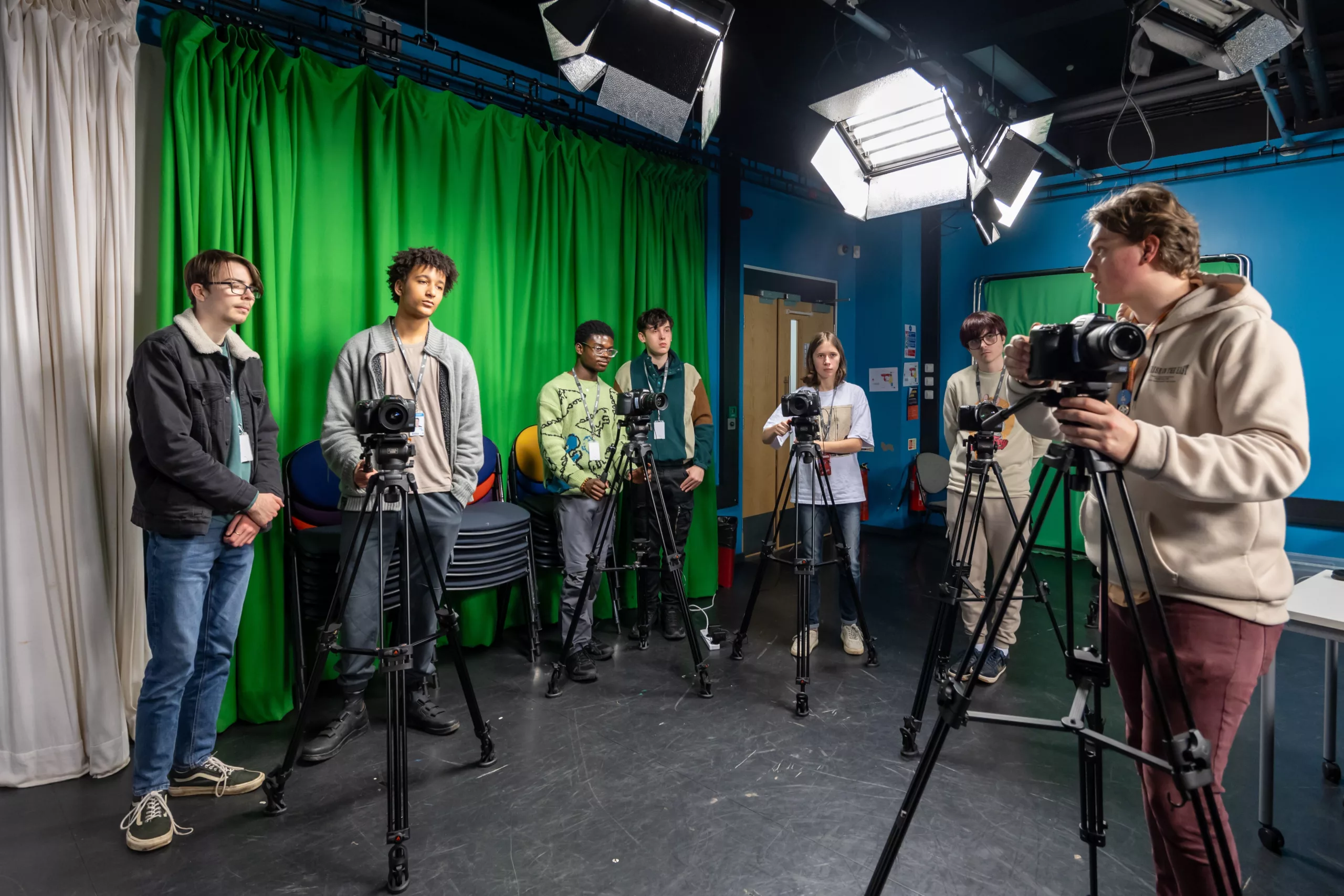 Media students handling professional video cameras in a green screen studio.