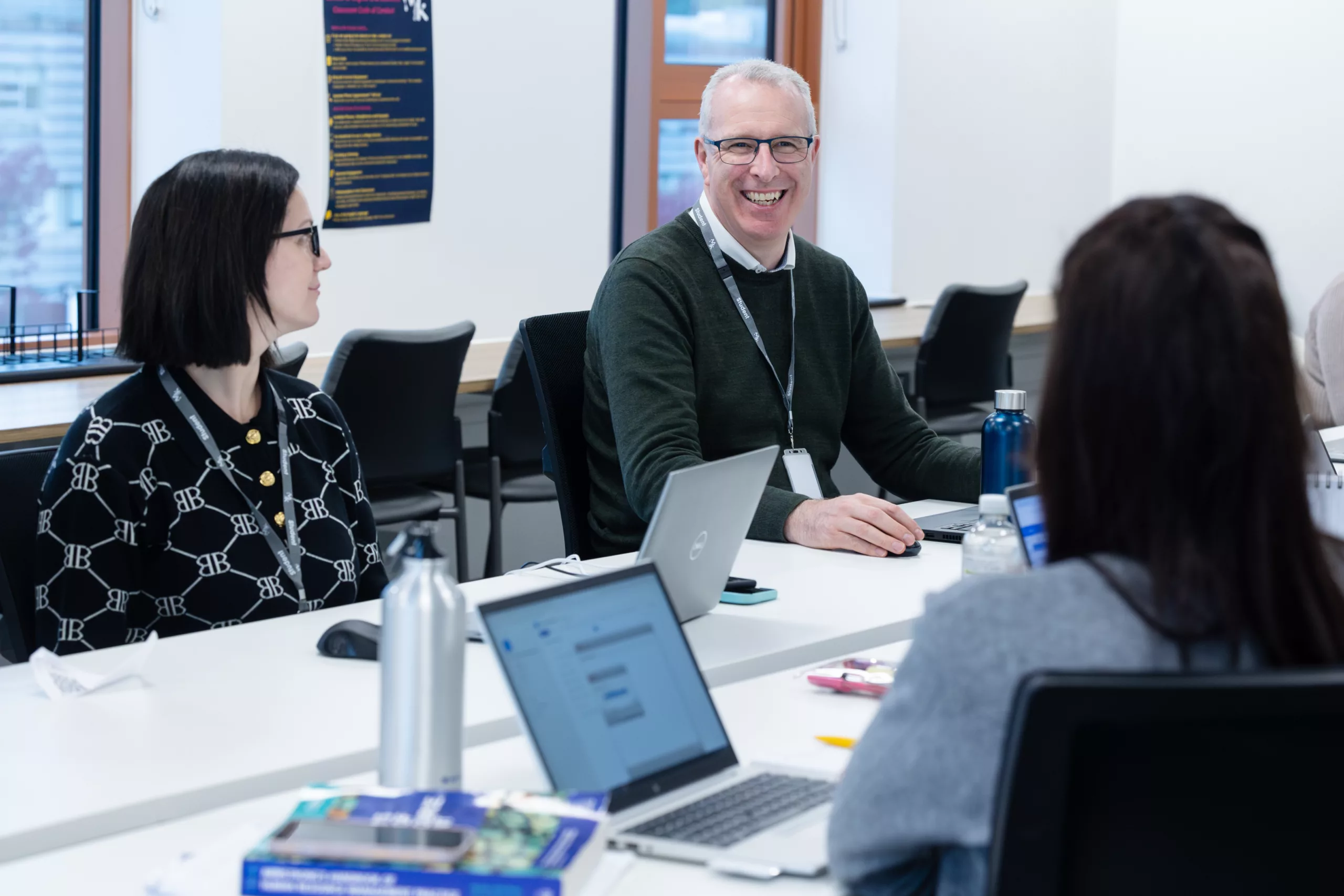 A man smiling to his two colleagues. All are sitting in front of their laptops.