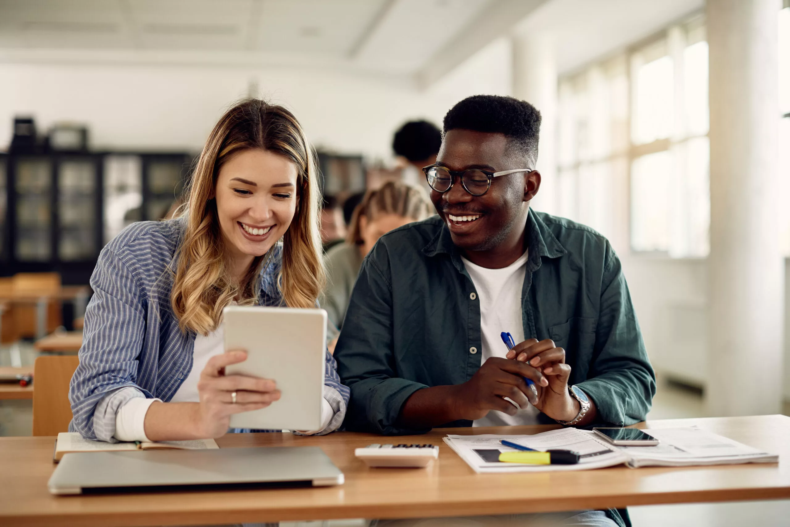 Happy college students use digital tablet during class in the classroom.