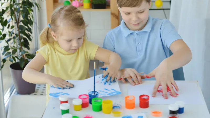 Two children playing with colourful fingerpaints.