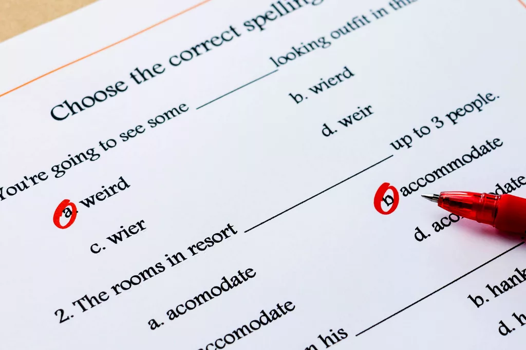 A photograph of a spelling test, with some multiple choice answers having been circled by a red pen. A red pen is partially pictured on the right-hand side.