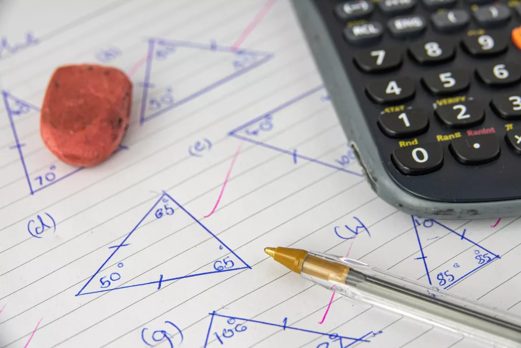 A photograph of triangles with degrees marked out drawn on a piece of paper. An orange eraser, a ballpoint pen and a calculator are partially included in the photo.