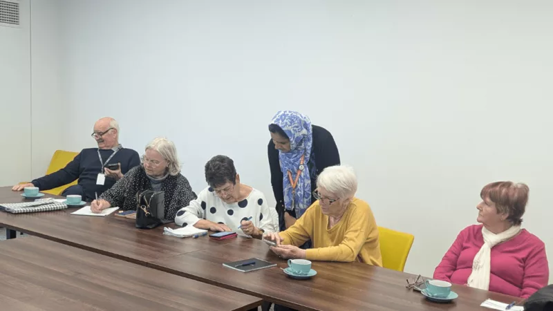 A photograph from a Tea and Tech event with a tutor assisting people with their digital problems.