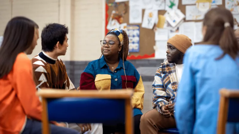People sitting on chairs in a circle, having a discussion.