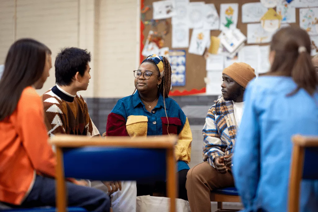 People sitting on chairs in a circle, having a discussion.